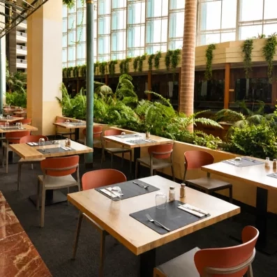 Une salle à manger lumineuse bordée d'une immense paroi vitrée et de plantes tropicales.