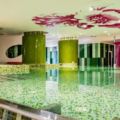 Une piscine intérieure élégante aux reflets verts, surplombée par un plafond décoré de motifs artistiques.
