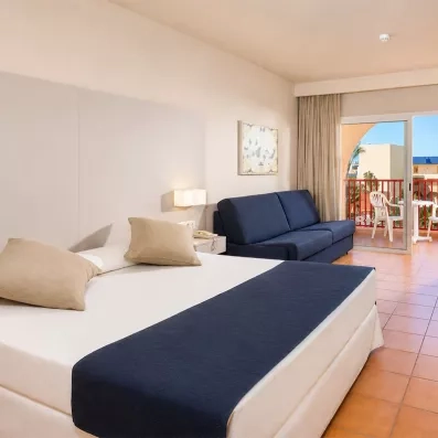 Une chambre d'hôtel avec un grand lit double, un canapé bleu et un balcon ensoleillé.