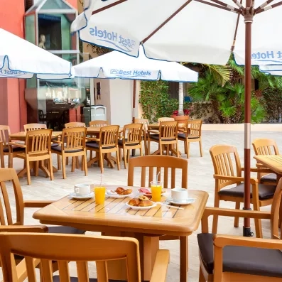 Une terrasse extérieure ensoleillée avec des tables en bois et des parasols blancs.