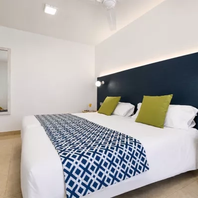 Une chambre d'hôtel lumineuse, avec un grand lit blanc souligné par un chemin de lit.