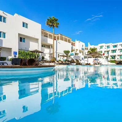 Une grande piscine aux eaux cristalline avec des palmiers d'un complexe hôtelier sous un ciel bleu.