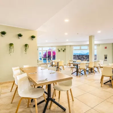 Une salle de restaurant spacieuse, baignée de lumière naturelle grâce à de grandes baies vitrées.
