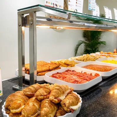 Un buffet de plats chauds et de viennoiseries présenté sous des lampes chauffantes.