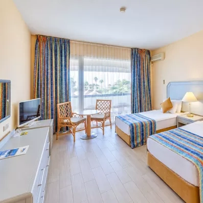 Une chambre lumineuse avec deux lits simples et un petit coin salon près de la fenêtre.