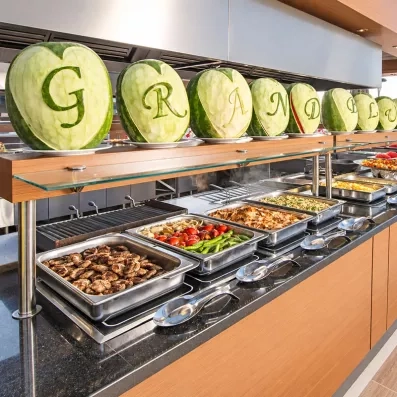 Un long buffet de plats chauds surmonté de pastèques sculptées au-dessus.