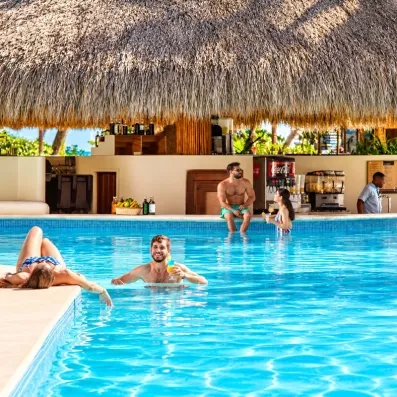 Des vacanciers dans une piscine couverte par une structure traditionnelle en chaume.