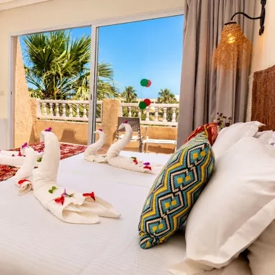 Chambre d'hôtel Welcome Meridiana Djerba avec lit décoré de serviettes en cygnes et vue sur balcon