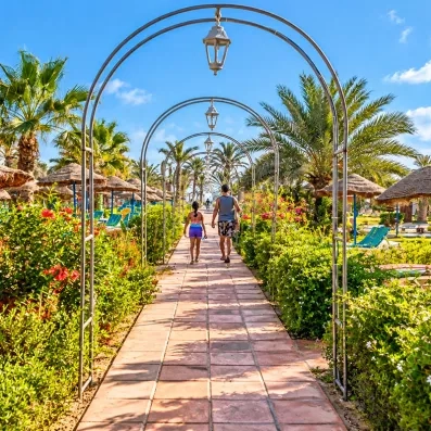 Allée pavée sous des arches métalliques dans les jardins de hôtel Welcome Meridiana Djerba