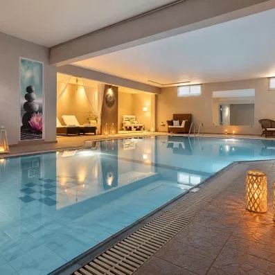 piscine intérieure, deux fauteuils au bord avec une petite table et une plante posée dessus, un canapé, un grand miroir, lumineux