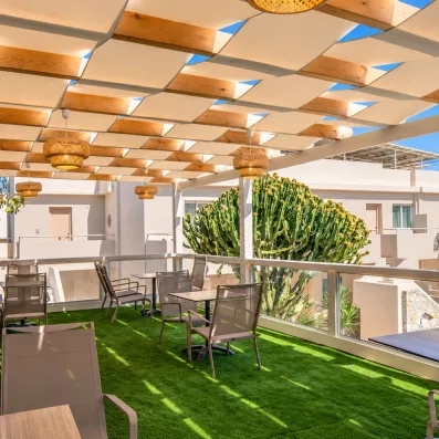 bar terrasse, luminaires tressés, grands cactus, plantes bâtiments blancs typiques, tables et chaises, sol en gazon