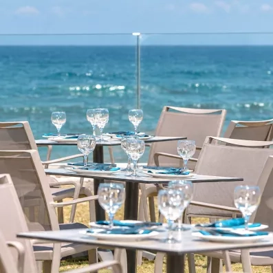tables carrées, chaises beiges, verres, terrasse avec vue sur la mer