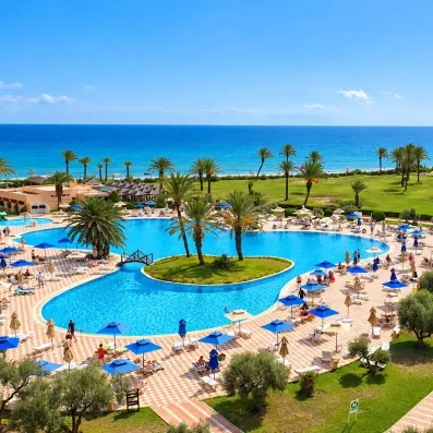 Grande piscine extérieure de l'hôtel Nour Palace Mahdia bordée de palmiers et vue mer