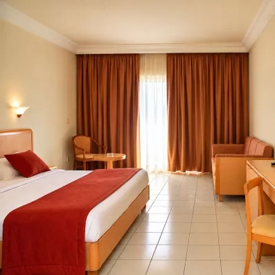 Chambre spacieuse avec grand lit, coin salon et rideaux rouges à l'hôtel Nour Palace Mahdia