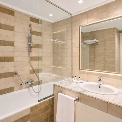 Salle de bains moderne avec baignoire et pare-douche en verre au Mondi Club Nozha Beach Resort & Spa.