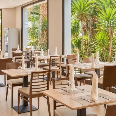 Salle de restaurant lumineuse avec baies vitrées donnant sur la végétation tropicale du Mondi Club Nozha Beach.