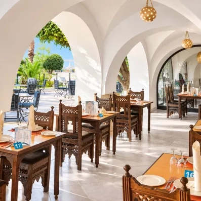 Restaurant à la carte d'inspiration orientale avec voûtes blanches et mobilier en bois sculpté au Mondi Club Nozha Beach.