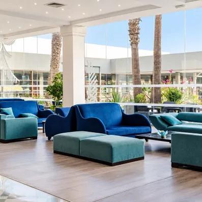Salon du hall de réception de l'hôtel Mondi Club One Resort Jockey avec de grands canapés bleus et de larges baies vitrées.