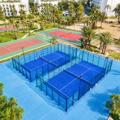 Terrains de padel bleus et courts de tennis de l'hôtel Mondi Club One Resort Jockey à Monastir entourés de palmiers.