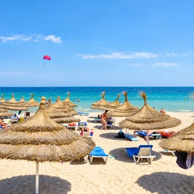 Plage privée de sable fin du Mondi Club One Resort Jockey à Monastir avec parasols en paille, transats et mer turquoise.