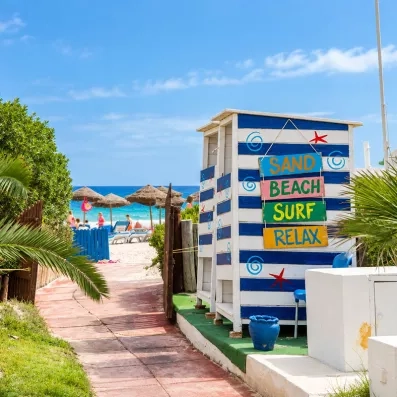 Chemin d'accès à la plage au Mondi Club One Resort Jockey avec cabine décorée de panneaux colorés "Sand Beach Surf Relax".