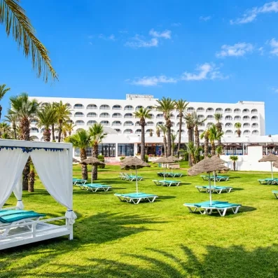Façade extérieure du bâtiment du Mondi Club One Resort Jockey à Monastir, vue depuis les jardins verdoyants avec lits de repos et transats.