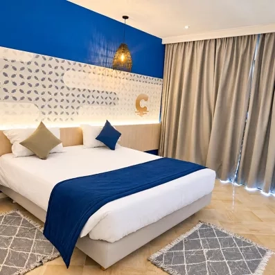 Chambre lumineuse de l'hôtel Mondi Club One Resort Jockey Monastir avec mur bleu et grand lit double