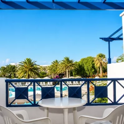 Un balcon aménagé avec une table et des chaises, offrant une vue sur les palmiers.