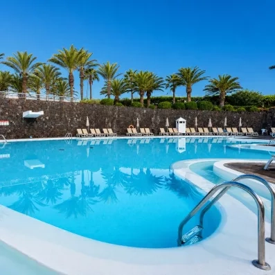 Une piscine calme au coucher du soleil, avec des palmiers et des transats en arrière-plan.