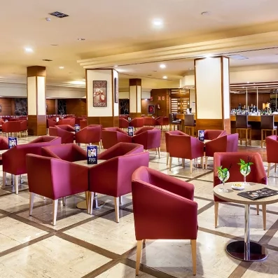 Un salon d'intérieur chic avec de nombreux fauteuils en velours rouge et de petites tables rondes.