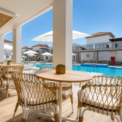 Une terrasse de restaurant ensoleillée avec des chaises en osier offrant une vue sur une piscine.