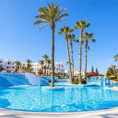 Piscine lagunaire avec pont en bois et palmiers au club tout inclus Seabel Aladin Djerba.