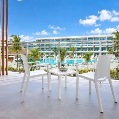 terrasse de la chambre avec vue piscine, table et deux chaises blanches, ciel bleu