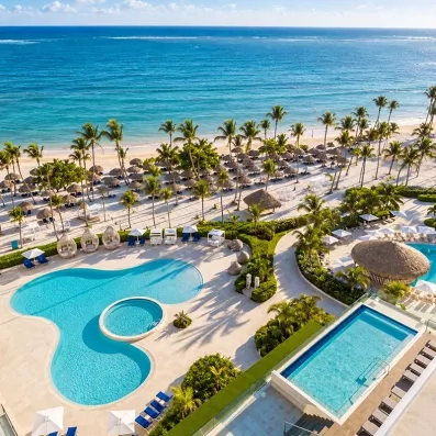 Une vue aérienne d’un complexe hôtelier, situé entre une piscine et une plage aux eaux turquoise.