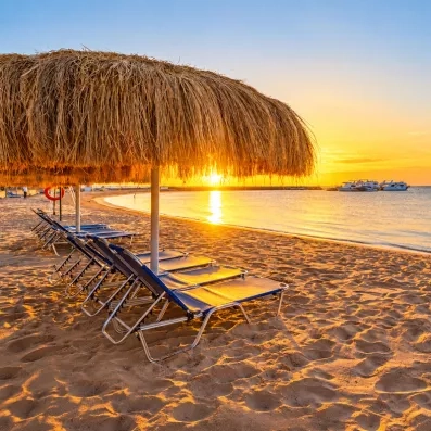 Coucher de soleil sur la plage privée du Mondi Club Seven Seas Jolie Bay à Hurghada avec transats et parasols en paille.
