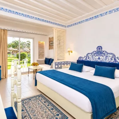 Chambre spacieuse avec lit king-size bleu et blanc et baie vitrée ouvrant sur le jardin au Mondi Club Shalimar
