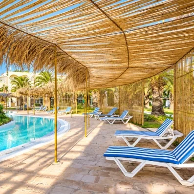 Transats à rayures bleues sous pergolas en paille au bord de la piscine du Mondi Club Shalimar.