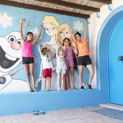 Enfants posant devant une fresque murale colorée lors d'une animation au Mondi Club Shems Monastir.