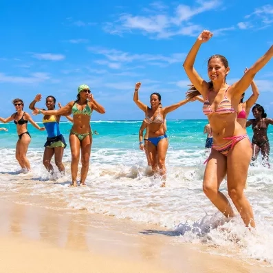 groupe de femmes dansant sur la plage de sable, océan en arrière plan, eau turquoise, ciel bleu