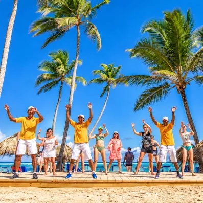cours de danse ou de gymnastique sur la plage avec des animateurs internationaux sur une plateforme, ciel bleu et palmiers