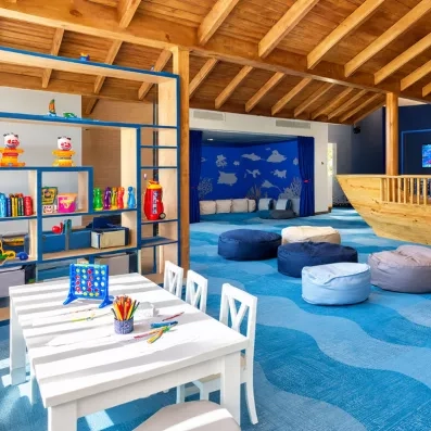 mini-club pour les petits, poufs disposés au centre, bateau en bois taille réelle sur la droite, étagères et table et chaises avec jeux posés dessus