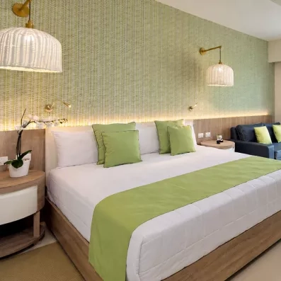 chambre double standard 1 lit avec dessus lit vert et un canapé lit, baie vitrée donnant sur un balcon avec table et chaises, vue sur le jardin et les palmiers