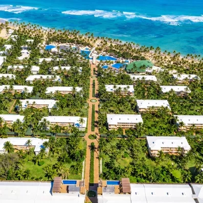 allée centrale partant de l'aquapark, passant par les boutiques et bars et menant à la plage et l'océan, végétation importante, nombreux palmiers, piscines, eau et ciel bleus