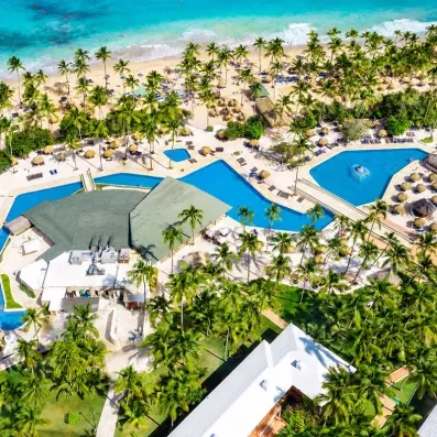 piscines avec accès direct sur la plage de sable, palmiers, végétation luxuriante, transats bleus et parasols paillote, pieds dans l'eau, océan et ciel bleus