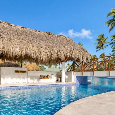 bar piscine, toit paillote, un homme et une femme en maillot de bain discutent dans la piscine en souriant et en buvant un cocktail, bouteilles dans le bar