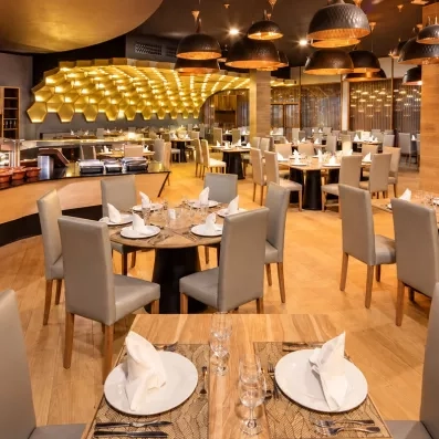 salle de restaurant chaises grises tables rondes en bois, parquet bois au sol et gros luminaires gris circulaires au plafond