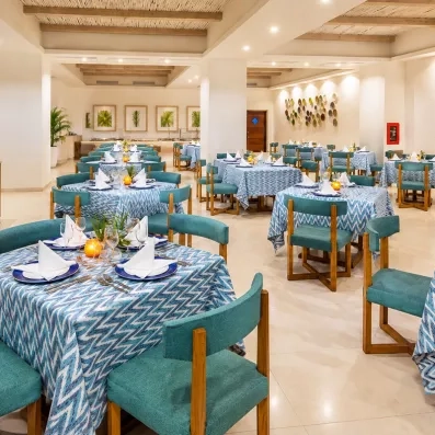 salle de restaurant tables carrées nappe bleue et chaises en velours vert, murs blancs avec quelques décorations latines