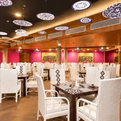 salle de restaurant tables carrées bois foncé et longues chaises blanches avec accoudoirs, murs rouges, plafond en bois