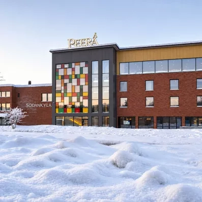 Façade enneigée du Mondi Club Peera Hotel Sodankylä en Laponie avec vitraux colorés.