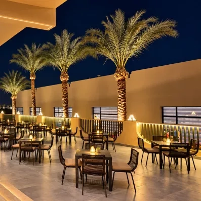 Terrasse de restaurant illuminée de nuit avec palmiers et mobilier moderne au Mondi Club, Égypte.